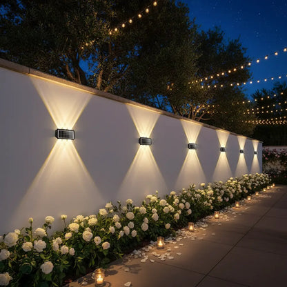 Decorative outdoor setting with white flowers, candles, and string lights against a white wall.
