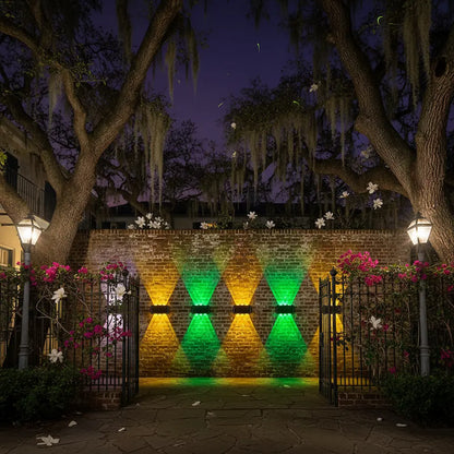 Brick wall with geometric lighting design at night, surrounded by trees and flowers.