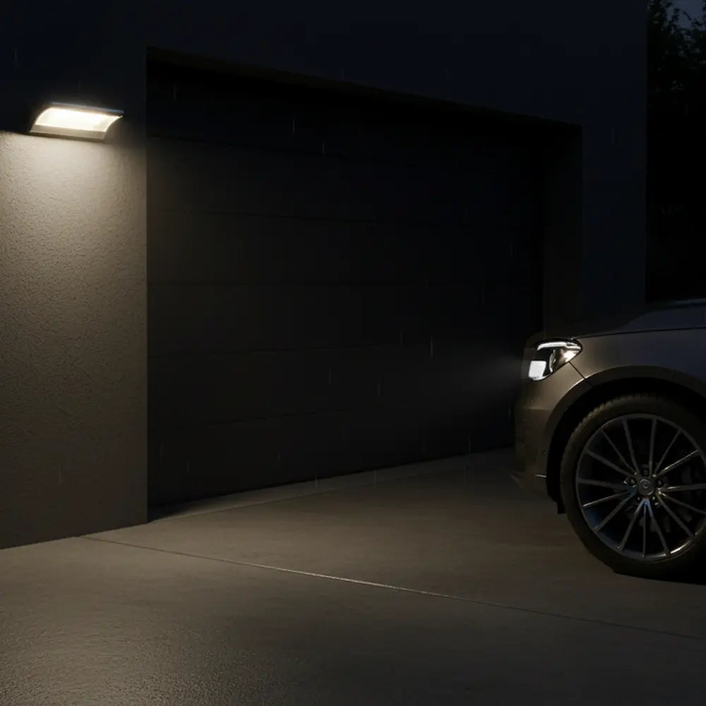 Car parked in a dark driveway with a wall-mounted light fixture.