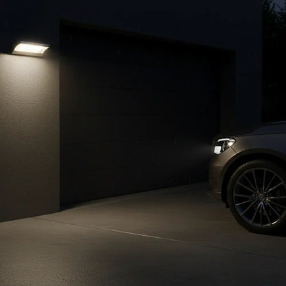 Car parked in a dark driveway with a wall-mounted light fixture.