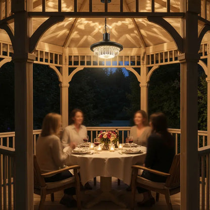 People dining under a gazebo at night with a chandelier hanging above.
