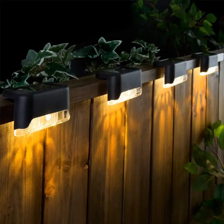 Solar-powered outdoor lights on a wooden fence with plants.