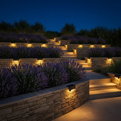 Staircase with stone walls and lavender plants illuminated by outdoor lighting at night.