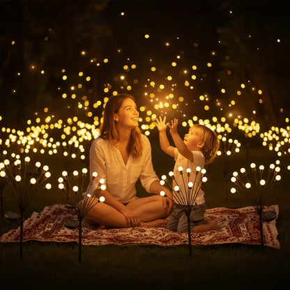 Woman and child sitting on a blanket surrounded by decorative lights in a dark setting