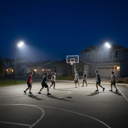 Basketball game on an outdoor court at night with streetlights illuminating the scene.