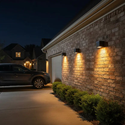 Car parked in a driveway with illuminated wall lights on a brick house exterior at night.