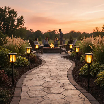 People gathered around a fire pit with illuminated pathway lights at sunset.