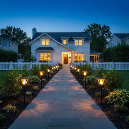 Evening view of a house with a well-lit pathway and garden lights.