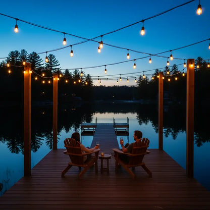 Two people sitting on a dock by a lake at night, illuminated by string lights.
