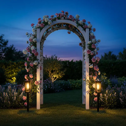 Floral archway decorated with lights in a garden setting at dusk.